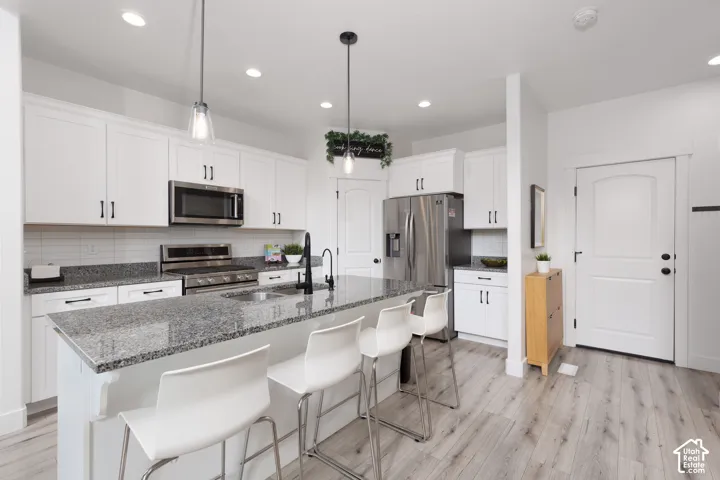White shaker cabinetry, stainless steel appliances, speckled stone countertops, a tile backsplash, and light wood-finish flooring