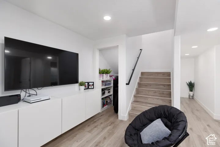 Recessed lighting illuminates wood-finish flooring, white walls, and a staircase with a black handrail