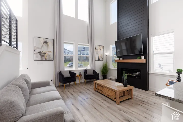 Double-height ceilings with high windows, a floor-to-ceiling black shiplap fireplace with an electric insert, wood-finish flooring, and black metal stair railings