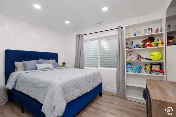 White wall paneling, recessed ceiling lighting, wood-finish flooring, and built-in shelving