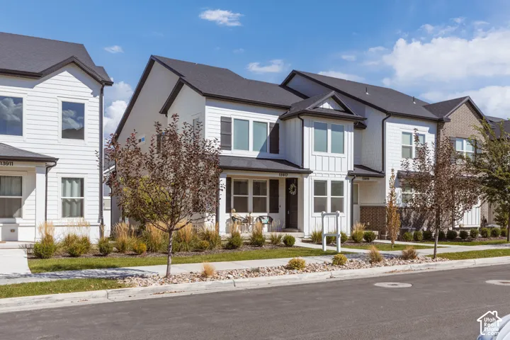 Contemporary exterior with white siding and dark trim, featuring multiple windows, a dark shingled roof, and a paved street