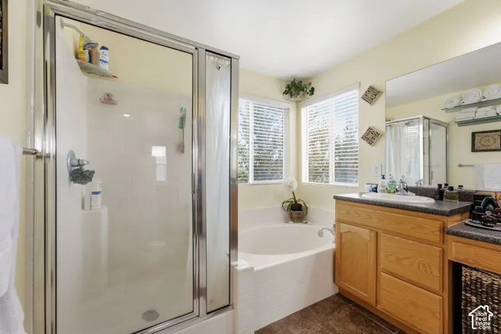 Enclosed shower with glass door, deep soaking tub, double windows with blinds, wood-finish vanity with integrated sink, and large wall-mounted mirror