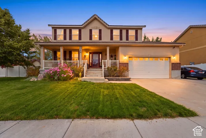 Two-story residence featuring a covered front porch with white railing, a two-car garage, brick accents, and a concrete driveway