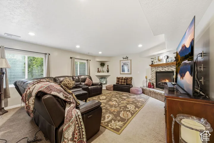 Recessed ceiling lighting, carpet flooring, a corner fireplace with a stone surround and wood mantle, and window treatments