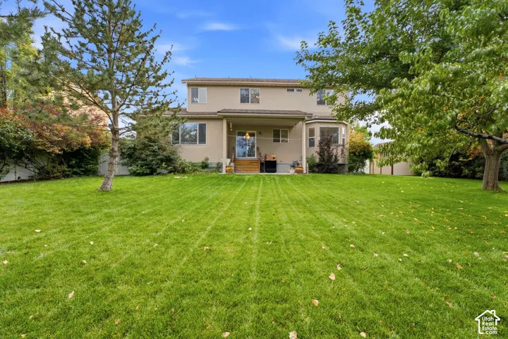 Expansive backyard featuring a manicured lawn, mature trees, and a two-story residence with a covered patio and bay window
