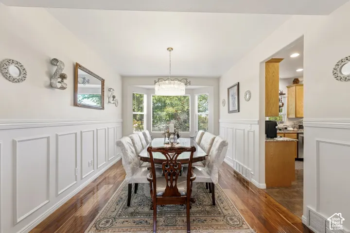 Wood-finish flooring, wainscoting, bay window, chandelier, and a framed opening to the kitchen