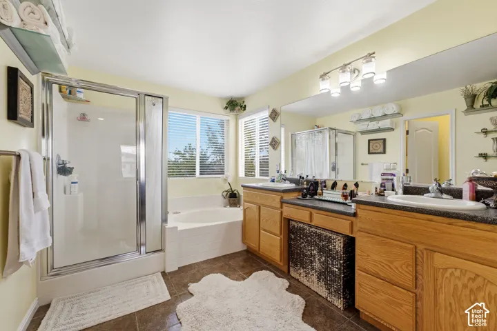 Dual vanity with integrated sinks, wood-finish cabinetry, built-in soaking tub, separate shower enclosure, and tiled flooring