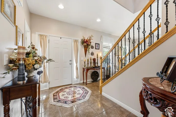 Foyer featuring tile flooring, a paneled entry door, a staircase with wrought iron balusters and wood handrail, and recessed lighting