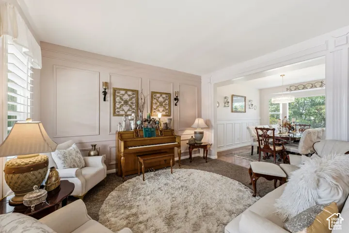 Wall paneling with integrated sconces, ceiling crown molding, window with plantation shutters, wood-finish flooring in adjacent room, and recessed lighting in adjacent room
