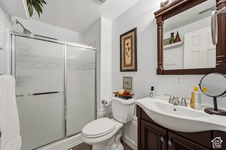 Integrated shower with frosted glass doors, a single vanity with a white basin and dark wood-finish cabinetry, and a toilet