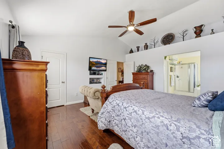 Vaulted ceiling with a ceiling fan, recessed wall shelving, wood-finish flooring, and an adjoining bathroom featuring a glass-enclosed shower