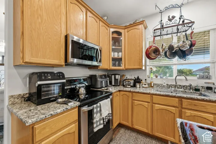 Wood-finish cabinetry, stainless steel microwave, integrated cooktop, stone-finish countertops, and a stainless steel sink with a high-arc faucet