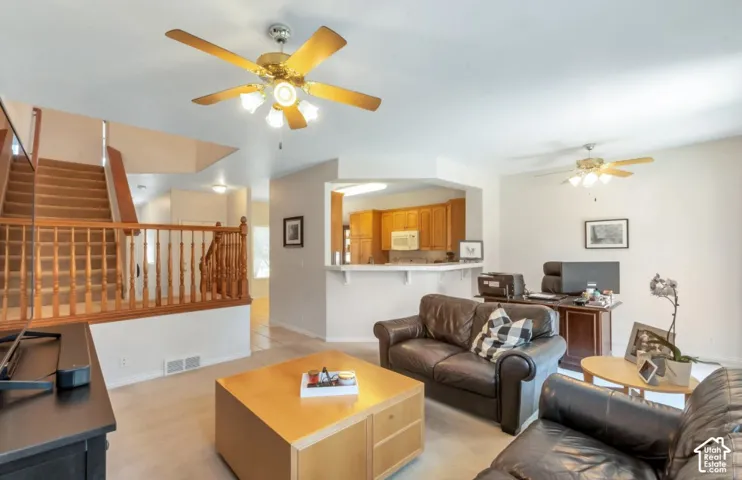 Carpeted flooring, ceiling fans with integrated lighting, wood-finish staircase with balusters, built-in breakfast bar, and wood-finish cabinetry