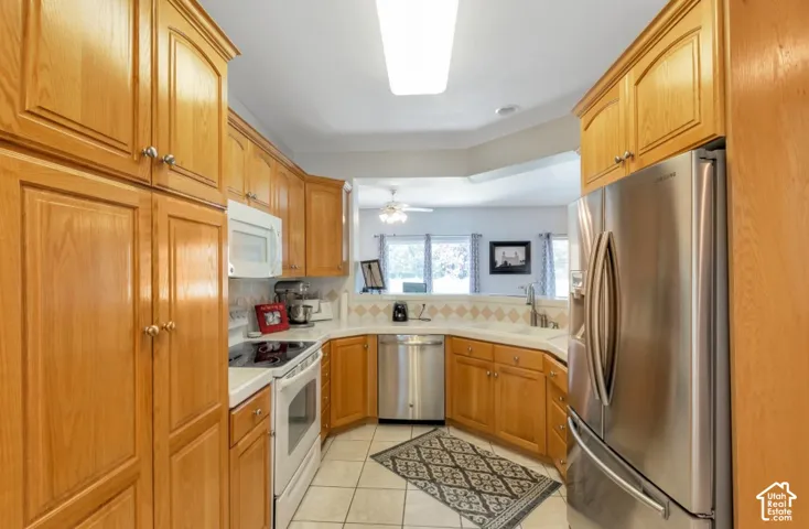 Wood-finish cabinetry, white tile flooring, stainless steel French door refrigerator, white range, and a dual-basin sink with a gooseneck faucet
