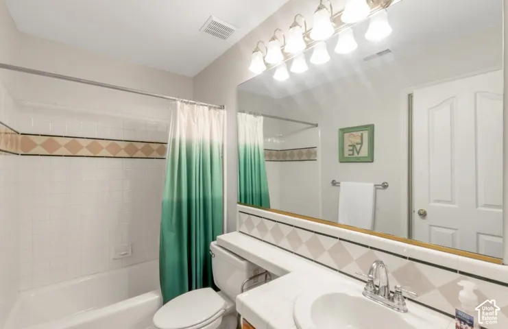 White subway tile shower with decorative accent band, white bathtub, vanity with integrated sink, chrome faucet, and expansive mirror with overhead lighting