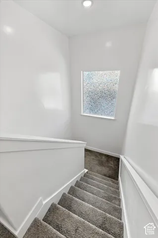 Stairwell featuring recessed lighting, a privacy window, white painted walls, and gray carpeted stairs with white risers