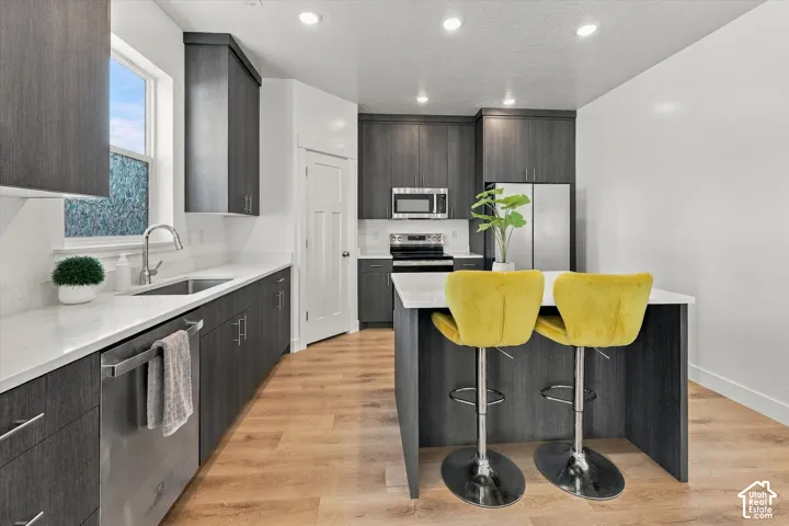 Modern kitchen featuring dark wood-finish cabinetry, light-colored countertops, stainless steel appliances, a kitchen island, and wood-finish flooring