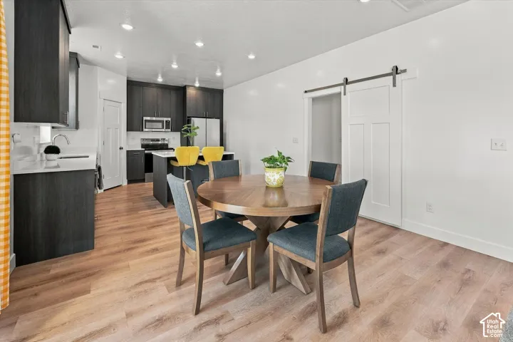 Open-concept living space with wood-finish flooring, a contemporary dark wood kitchen, white quartz countertops, stainless steel appliances, and a modern barn door