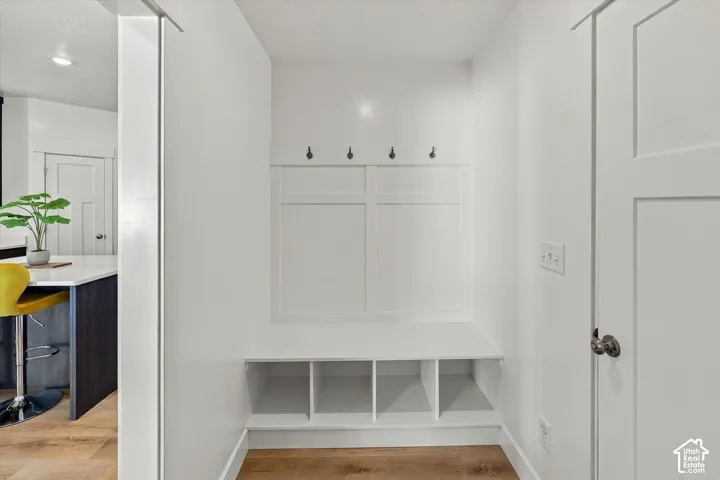 Built-in entryway bench with storage cubbies and wall hooks, wood-finish flooring, white panel door, and recessed lighting