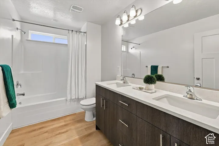 Dual vanity with integrated sinks, wood-finish cabinetry, a large mirror, and a full bathtub with an overhead window