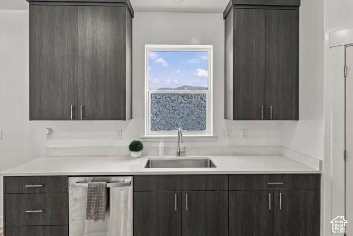 Dark wood-finish cabinetry, light-toned countertops, stainless steel sink with faucet, and integrated dishwasher