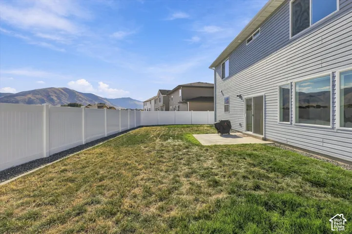 Expansive fenced backyard featuring a concrete patio, sliding glass door access, and mountain scenery