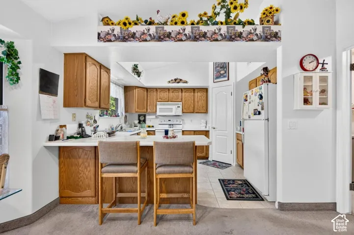 Kitchen featuring wood cabinetry, white countertops, white appliances, and tile flooring