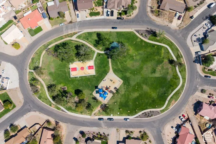 Circular green space featuring a basketball court, playground equipment with a blue shade structure, mature trees, and paved walking paths