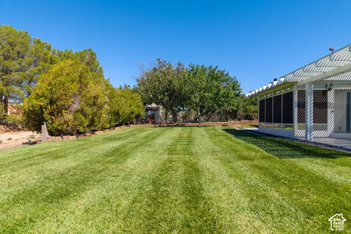 Expansive lawn with manicured grass, mature trees, and a covered patio featuring a white pergola