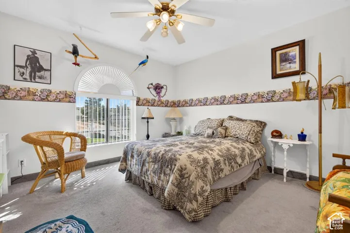 Spacious bedroom with carpet flooring, ceiling fan with brass fixtures, and abundant natural light from arched transom window
