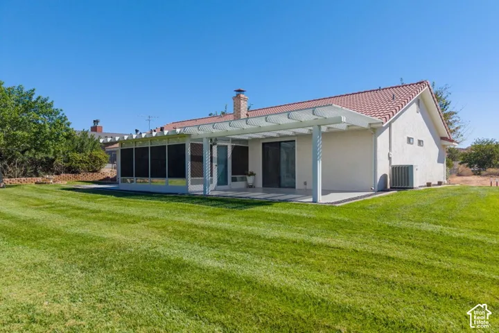 Expansive green lawn with a covered patio featuring a white pergola, brick chimney, and red tile roof