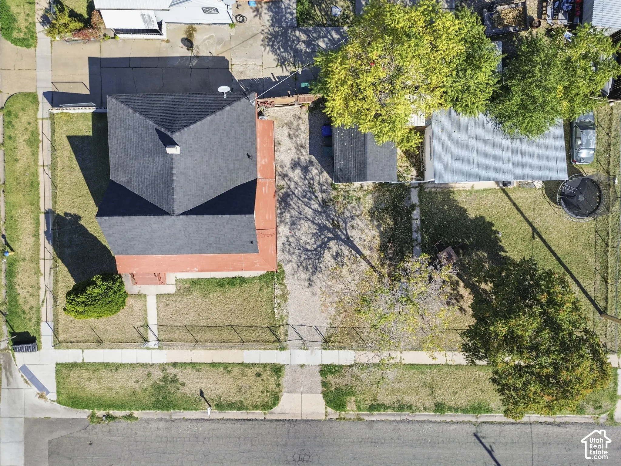 Gabled roofline, fenced perimeter, paved driveway, mature trees, and sidewalk access