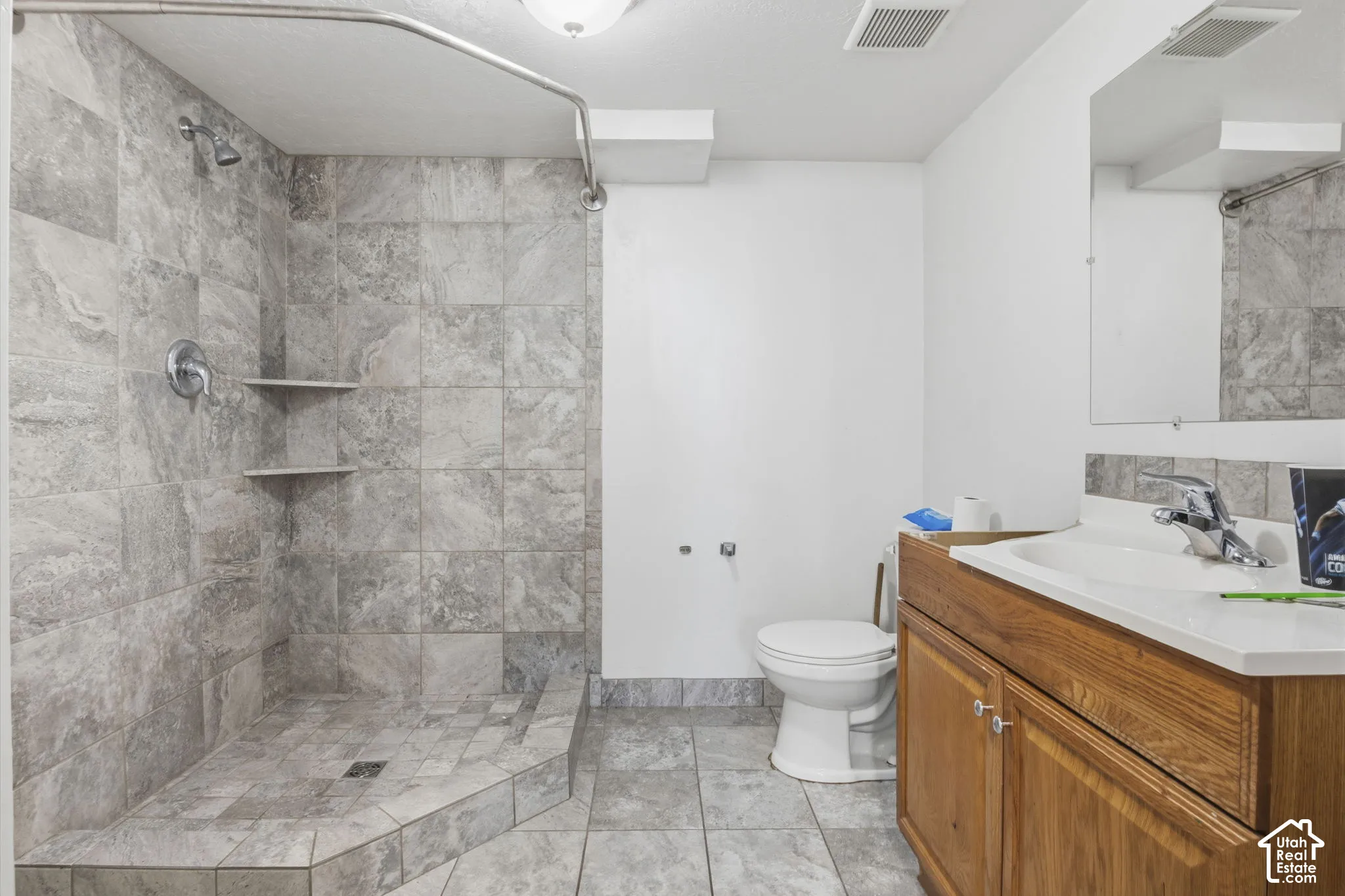 Bathroom featuring a tiled shower with integrated shelving, chrome shower fixtures, a wood-finish vanity with an integrated sink, and a chrome faucet