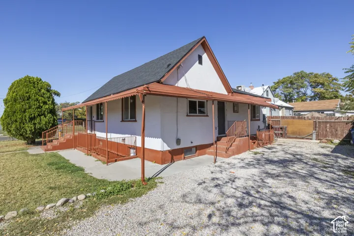White stucco exterior with orange trim, covered porch, multiple entry points, gravel driveway, and a fenced yard