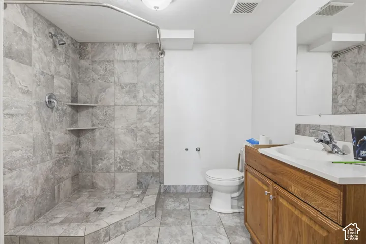 Bathroom featuring a tiled shower with integrated shelving, chrome shower fixtures, a wood-finish vanity with an integrated sink, and a chrome faucet