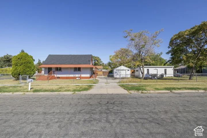 Fenced lot featuring a white exterior structure with a covered entry, a detached shed, and mature trees