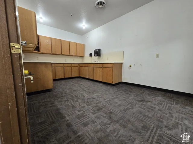 Open room featuring a corner sink, extensive cabinetry, and patterned carpet flooring