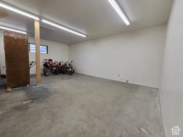 Concrete flooring with white walls, exposed wood support beam, and overhead fluorescent lighting