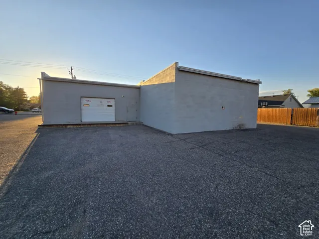 Paved lot with a commercial building featuring a roll-up door and a wood fence