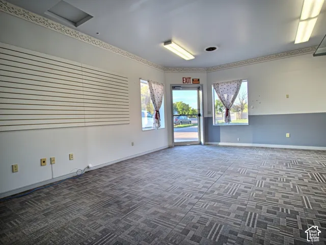 Recessed ceiling lights, fluorescent lighting, patterned carpet flooring, slatwall paneling, and a glass-paneled entry door