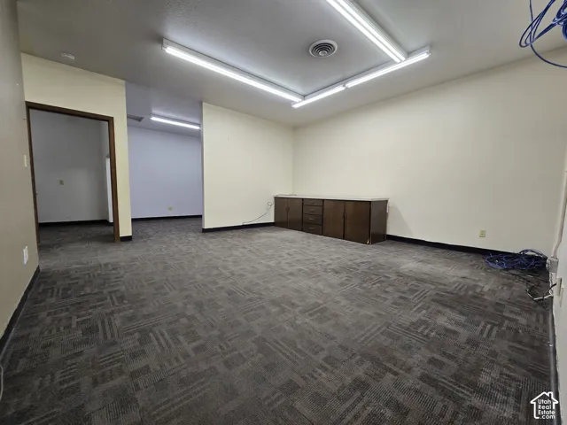 Recessed fluorescent lighting fixtures, light-colored walls, patterned carpeting, built-in dark wood cabinetry with a light countertop