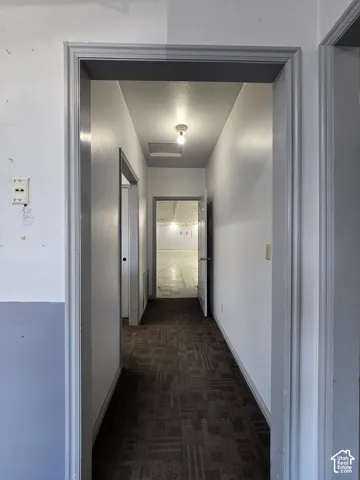 Hallway with patterned carpet flooring, white walls, and overhead lighting