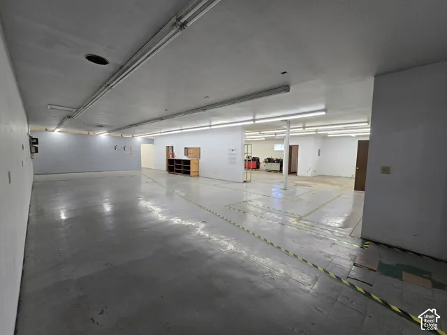 Expansive open space featuring concrete flooring, white painted walls, and fluorescent ceiling lighting