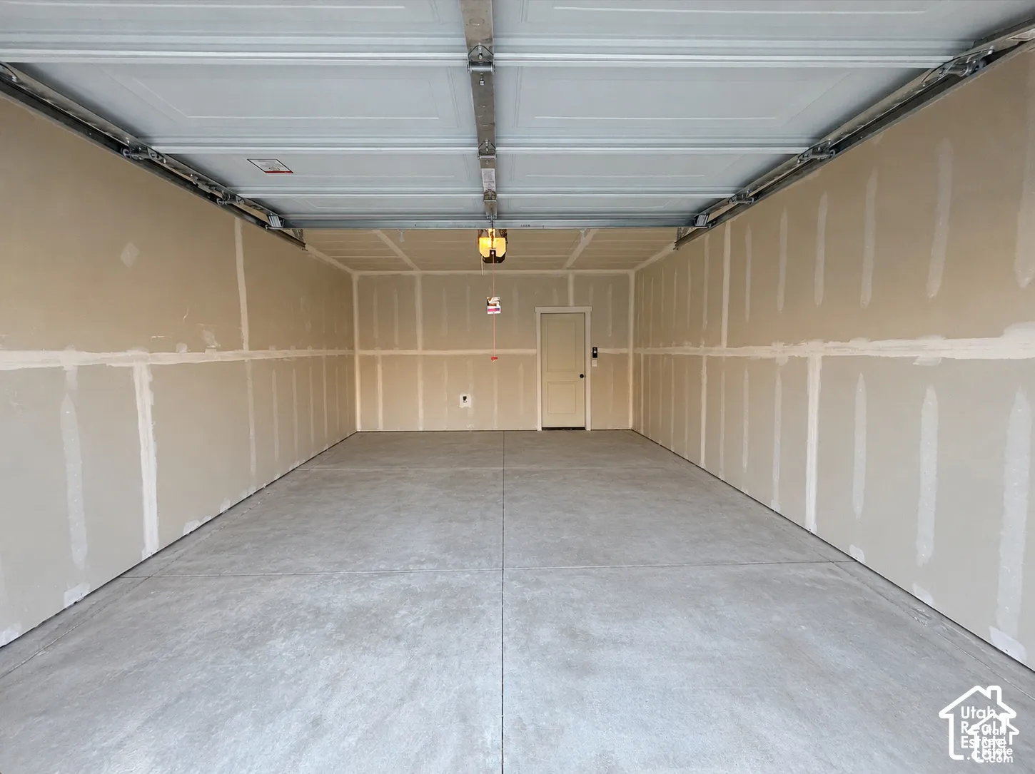 Concrete floor garage with unpainted drywall, overhead lighting, and an interior access door