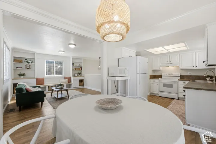 Open-concept living space featuring wood-finish flooring, white built-in shelving, white cabinetry, and a woven pendant light fixture