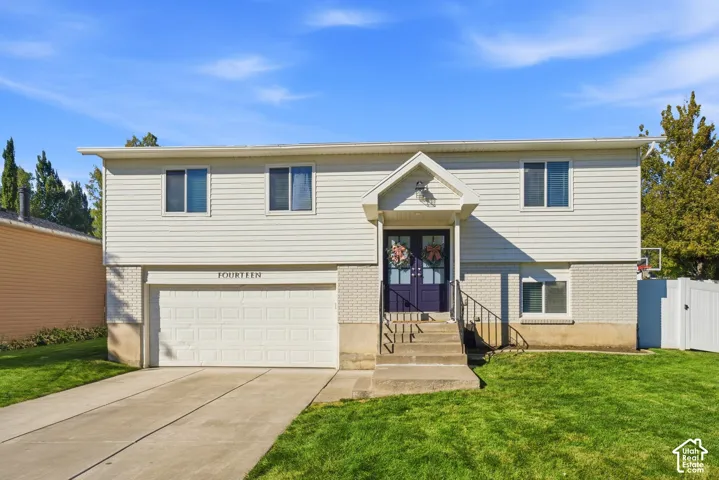 Split-level residence featuring white siding, a two-car garage, and a concrete driveway