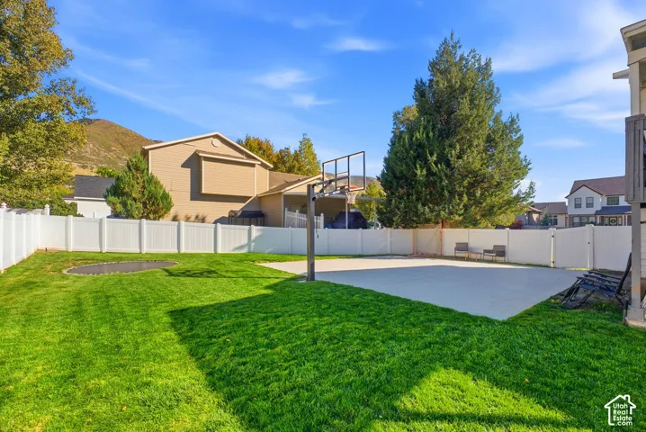 Expansive backyard with a manicured lawn, a large concrete pad, and a white privacy fence