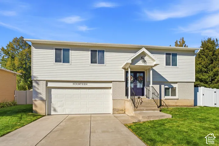 Split-level residence featuring white siding, a two-car garage, and a covered entry