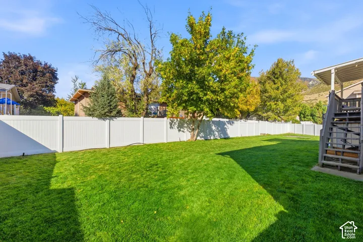 Expansive lawn area with a white privacy fence and mature trees