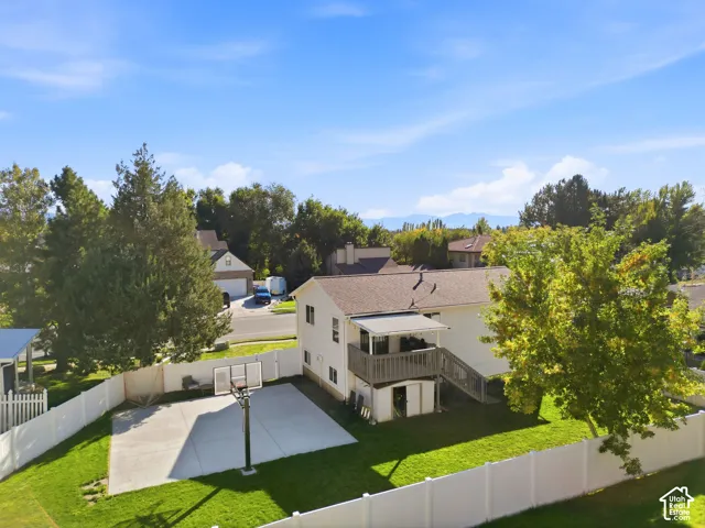 Expansive backyard featuring a concrete sport court, lush green lawn, mature trees, and a white privacy fence